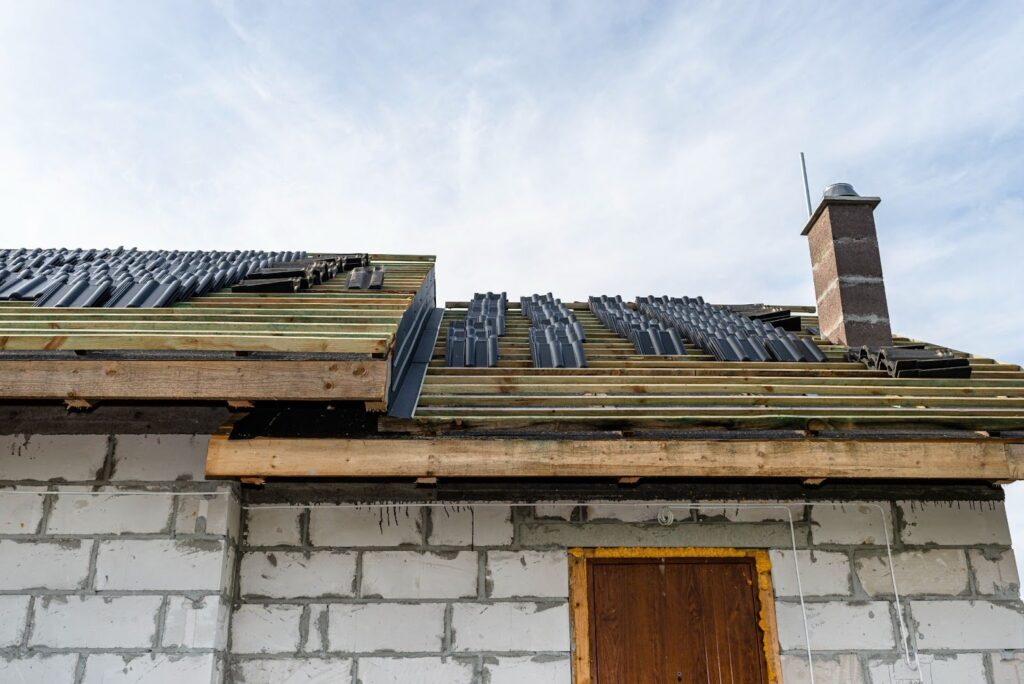 Ceramic roof tiles stacked on battens, ready for installation on a boarded roof.